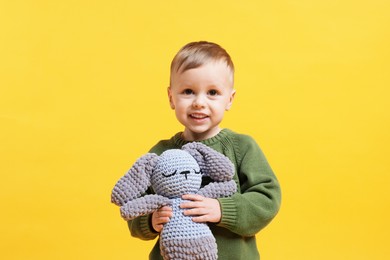 Cute little boy with toy bunny on yellow background