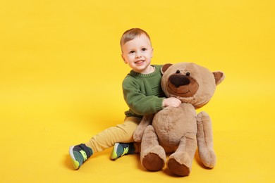 Photo of Cute little boy with toy bear on yellow background. Space for text