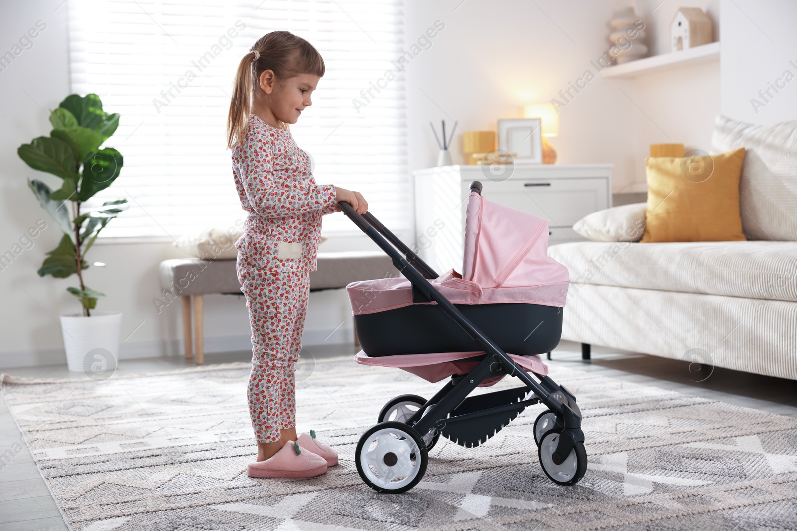 Photo of Cute little girl with doll stroller at home