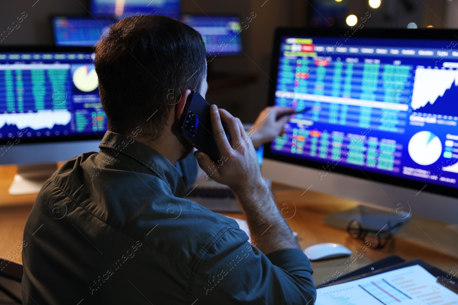 Photo of Financial trading specialist talking on phone in office at night, back view