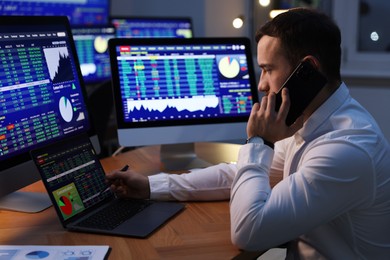 Photo of Financial trading specialist talking on phone in office at night