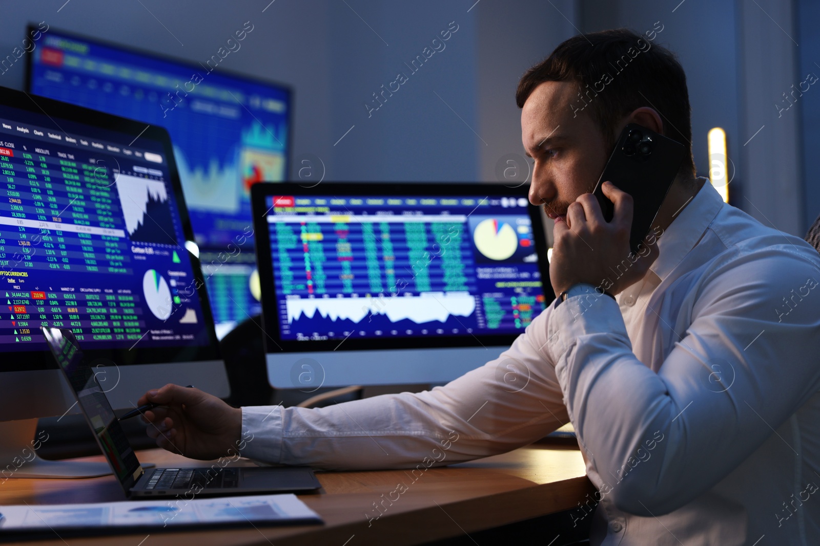 Photo of Financial trading specialist talking on phone in office at night