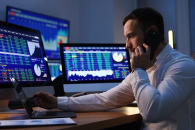 Photo of Financial trading specialist talking on phone in office at night