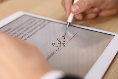 Photo of Electronic signature. Man using stylus and tablet at table, closeup