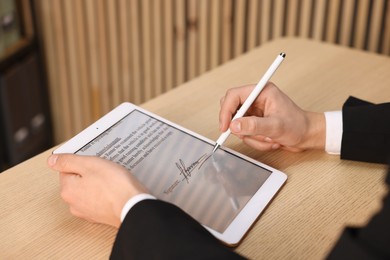 Photo of Electronic signature. Man using stylus and tablet at wooden table, closeup