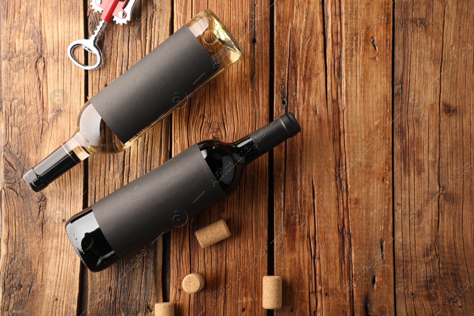 Bottles of wine, corks and wing corkscrew on wooden table, flat lay. Space for text Photo of Bottles of wine, corks and wing corkscrew on wooden table, flat lay. Space for text