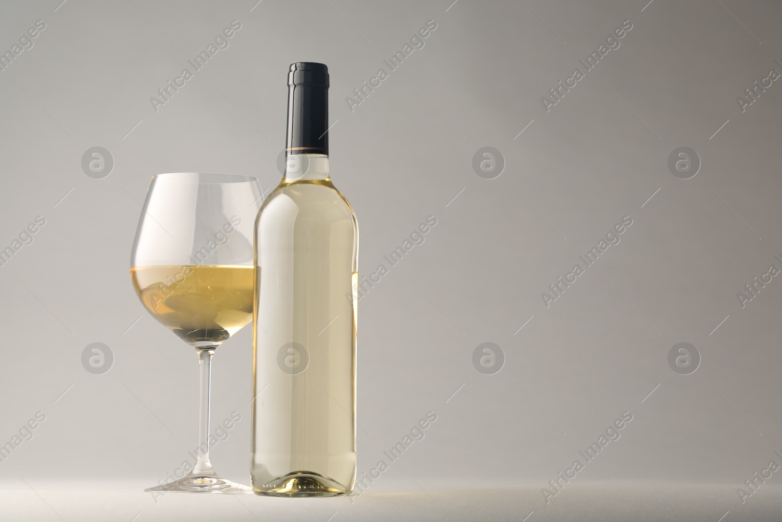 Tasty white wine in glass and bottle on light grey background, space for text Photo of Tasty white wine in glass and bottle on light grey background, space for text