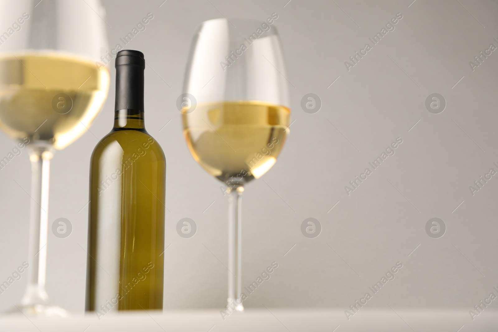 Tasty white wine in glasses and bottle on light grey background, low angle view. Space for text Photo of Tasty white wine in glasses and bottle on light grey background, low angle view. Space for text
