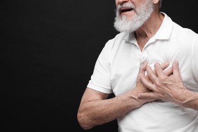 Photo of Heart attack. Senior man suffering from pain in chest on black background, closeup. Space for text