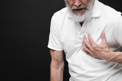 Heart attack. Senior man suffering from pain in chest on black background, closeup. Space for text