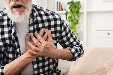 Photo of Heart attack. Senior man suffering from pain in chest on sofa at home, closeup