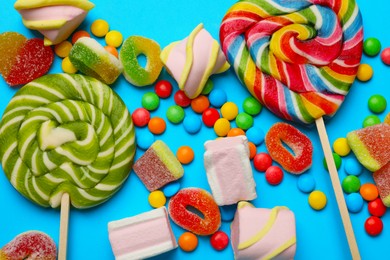 Many different tasty candies and marshmallows on light blue background, flat lay