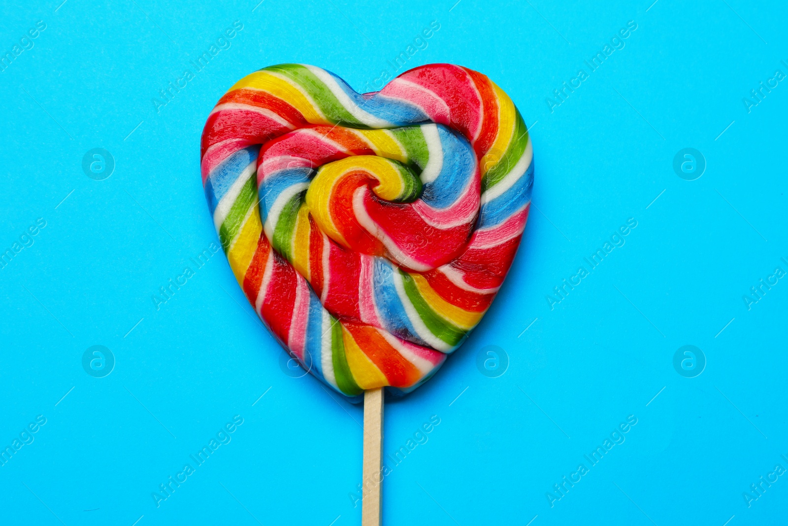 Photo of Tasty heart shaped lollipop on light blue background, top view