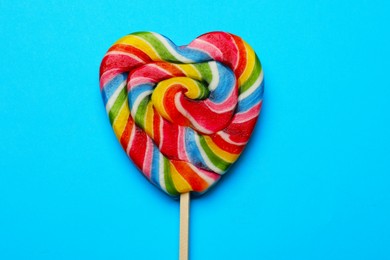 Tasty heart shaped lollipop on light blue background, top view