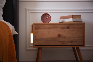 Photo of Glowing modern LED lamp on wooden bedside table indoors