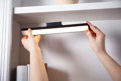 Photo of Woman putting modern LED lamp onto shelf indoors, closeup