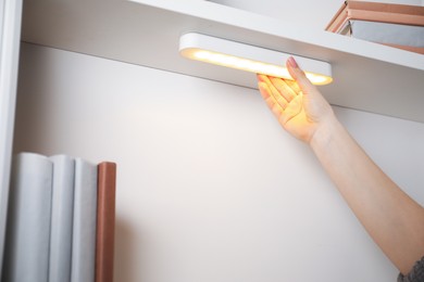 Photo of Woman putting modern LED lamp onto shelf indoors, closeup