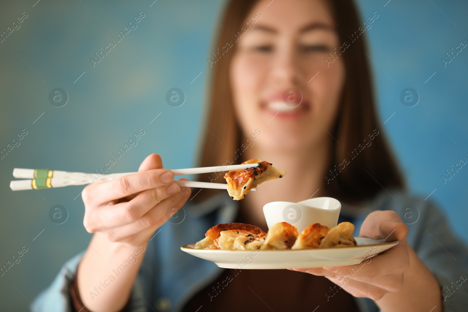 Photo of Woman holding tasty fried gyoza (dumplings) on light blue background, selective focus