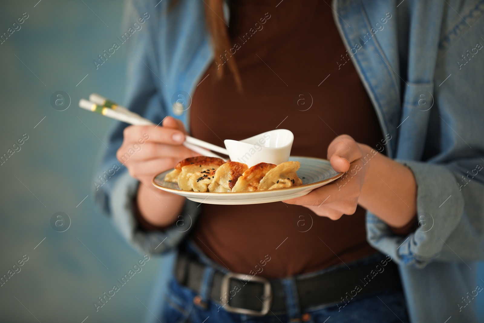 Photo of Woman holding tasty fried gyoza (dumplings) on light blue background, closeup