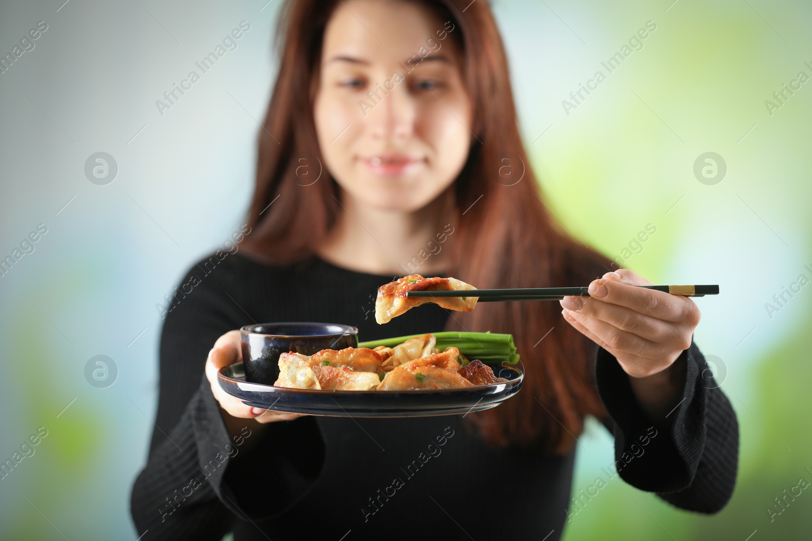 Photo of Woman holding tasty fried gyoza (dumplings) on blurred background, selective focus