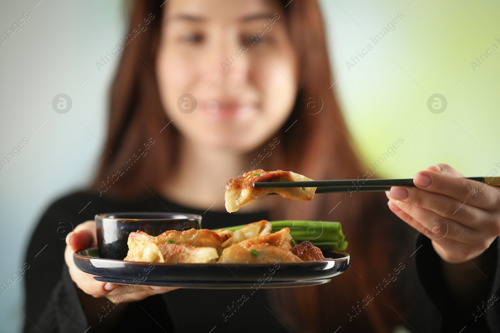 Photo of Woman holding tasty fried gyoza (dumplings) on blurred background, selective focus