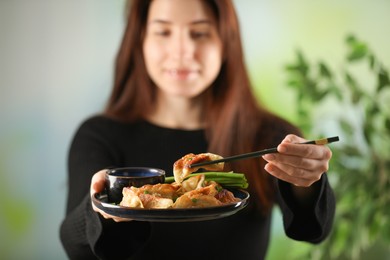 Photo of Woman holding tasty fried gyoza (dumplings) on blurred background, selective focus