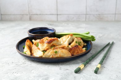 Tasty fried gyoza (dumplings) and soy sauce on light grey table, closeup