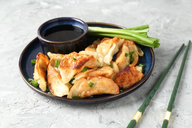 Tasty fried gyoza (dumplings) and soy sauce on light grey table, closeup