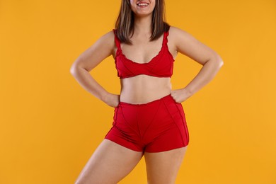 Photo of Woman in red underwear on orange background, closeup. Cellulite problem