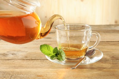 Photo of Pouring freshly brewed tea from teapot into glass cup on wooden table, closeup