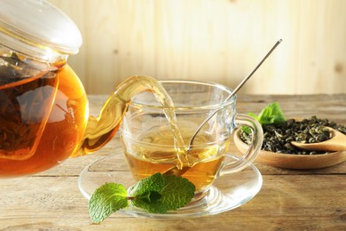 Photo of Pouring freshly brewed tea from teapot into glass cup on wooden table, closeup