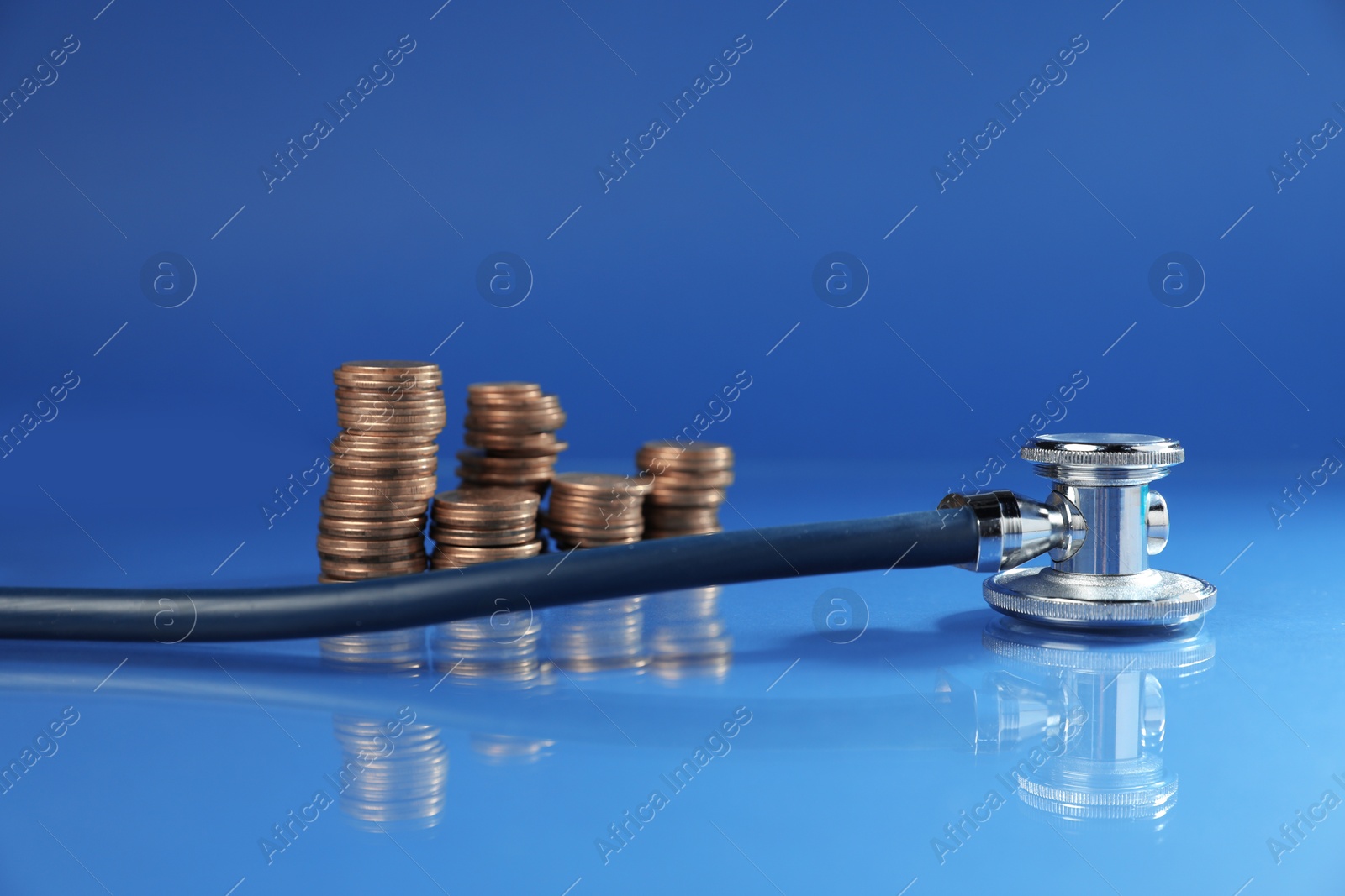 Stethoscope and coins on glass surface against blue background. Medical tool Photo of Stethoscope and coins on glass surface against blue background. Medical tool