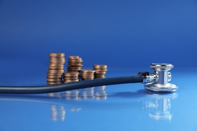 Photo of Stethoscope and coins on glass surface against blue background. Medical tool