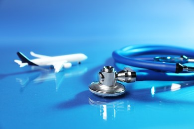 Photo of Stethoscope and airplane model on glass surface against blue background, closeup
