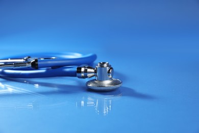 Photo of Stethoscope on glass surface against blue background, closeup. Space for text