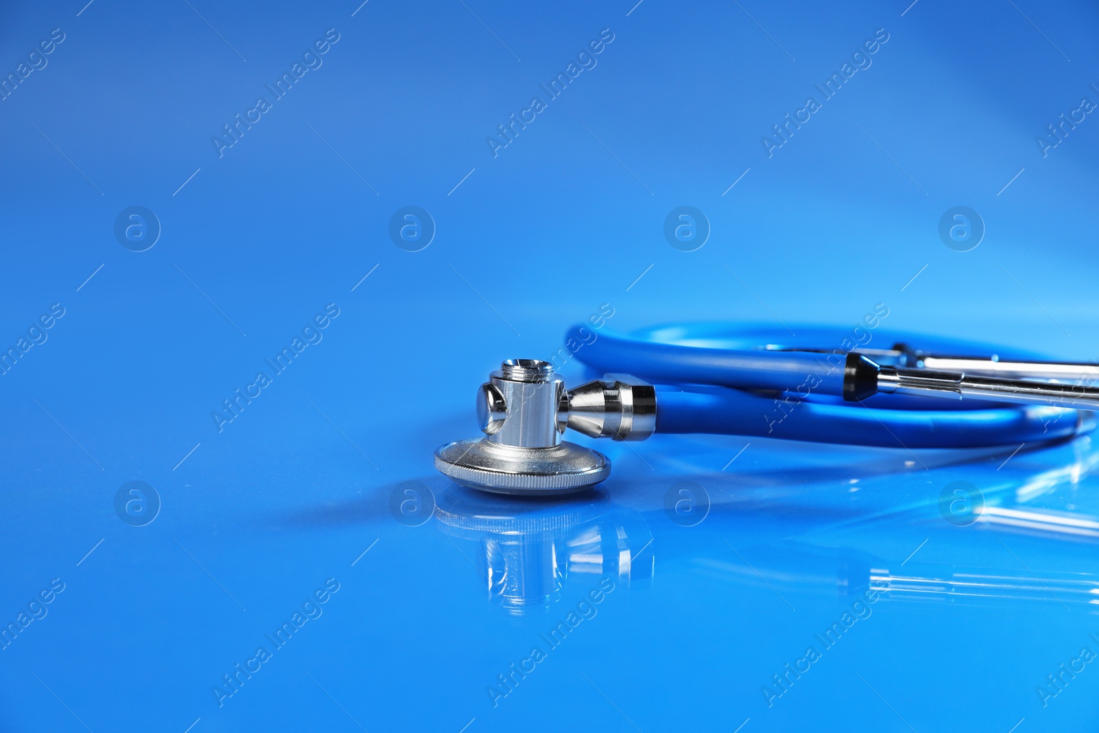 Stethoscope on glass surface against blue background, closeup. Space for text Photo of Stethoscope on glass surface against blue background, closeup. Space for text