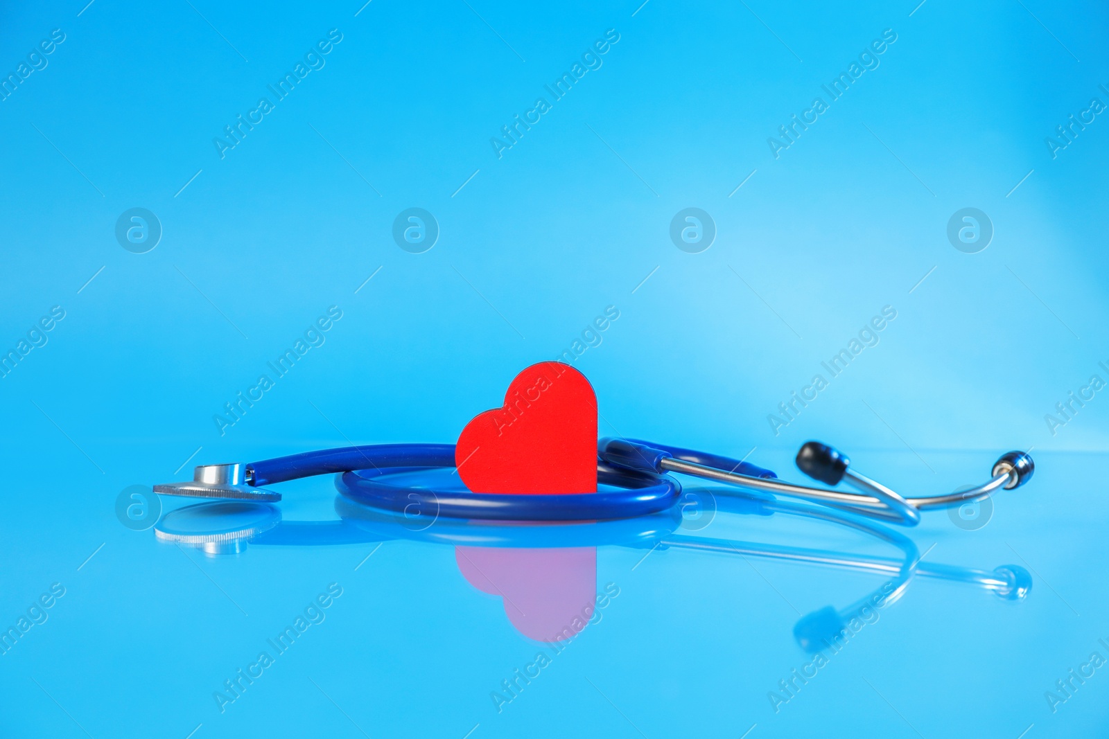 Stethoscope and red decorative heart on glass surface against light blue background Photo of Stethoscope and red decorative heart on glass surface against light blue background