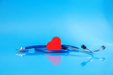 Photo of Stethoscope and red decorative heart on glass surface against light blue background