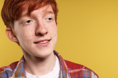 Smiling teenage boy with freckles on yellow background, closeup. Space for text