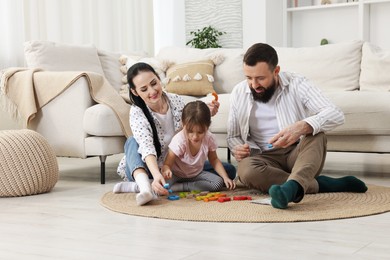 Photo of Cute little girl and her parents playing with set of colorful figures at home