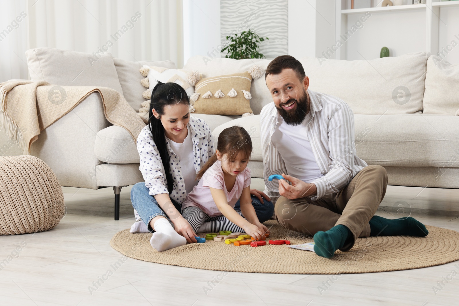 Photo of Cute little girl and her parents playing with set of colorful figures at home