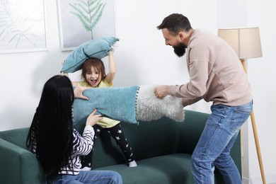 Photo of Cute little girl and her parents having fun while fighting with pillows at home