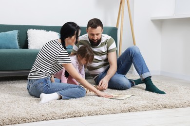 Photo of Cute little girl and her parents playing with set of wooden figures at home