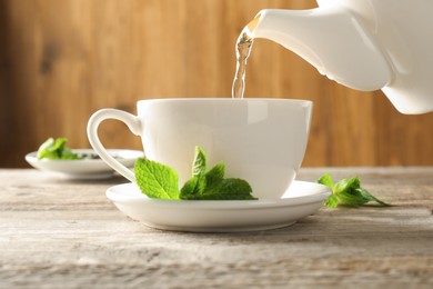 Photo of Pouring freshly brewed tea from teapot into cup at wooden table, closeup