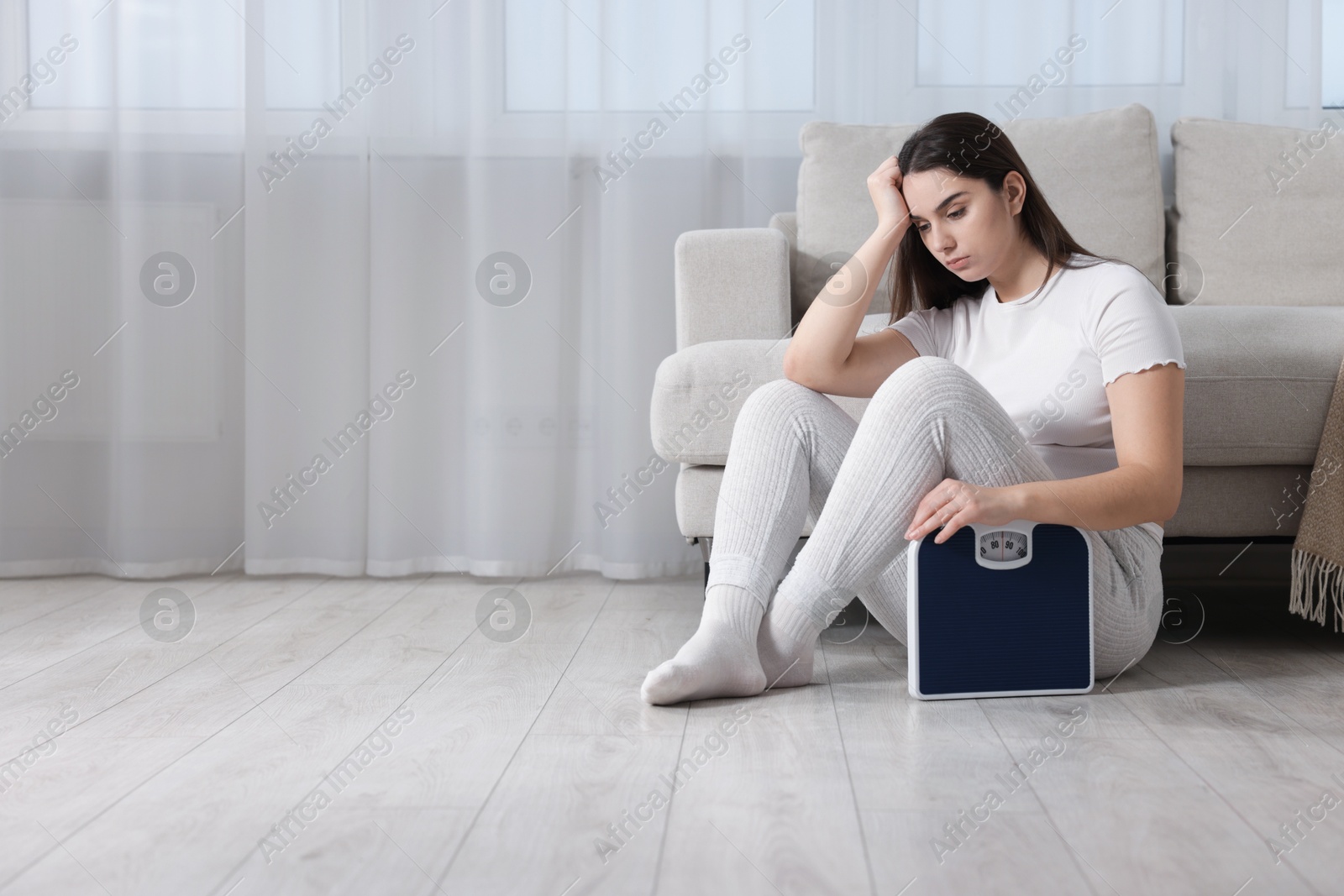 Photo of Depressed woman with scales on floor at home, space for text. Bulimia problem