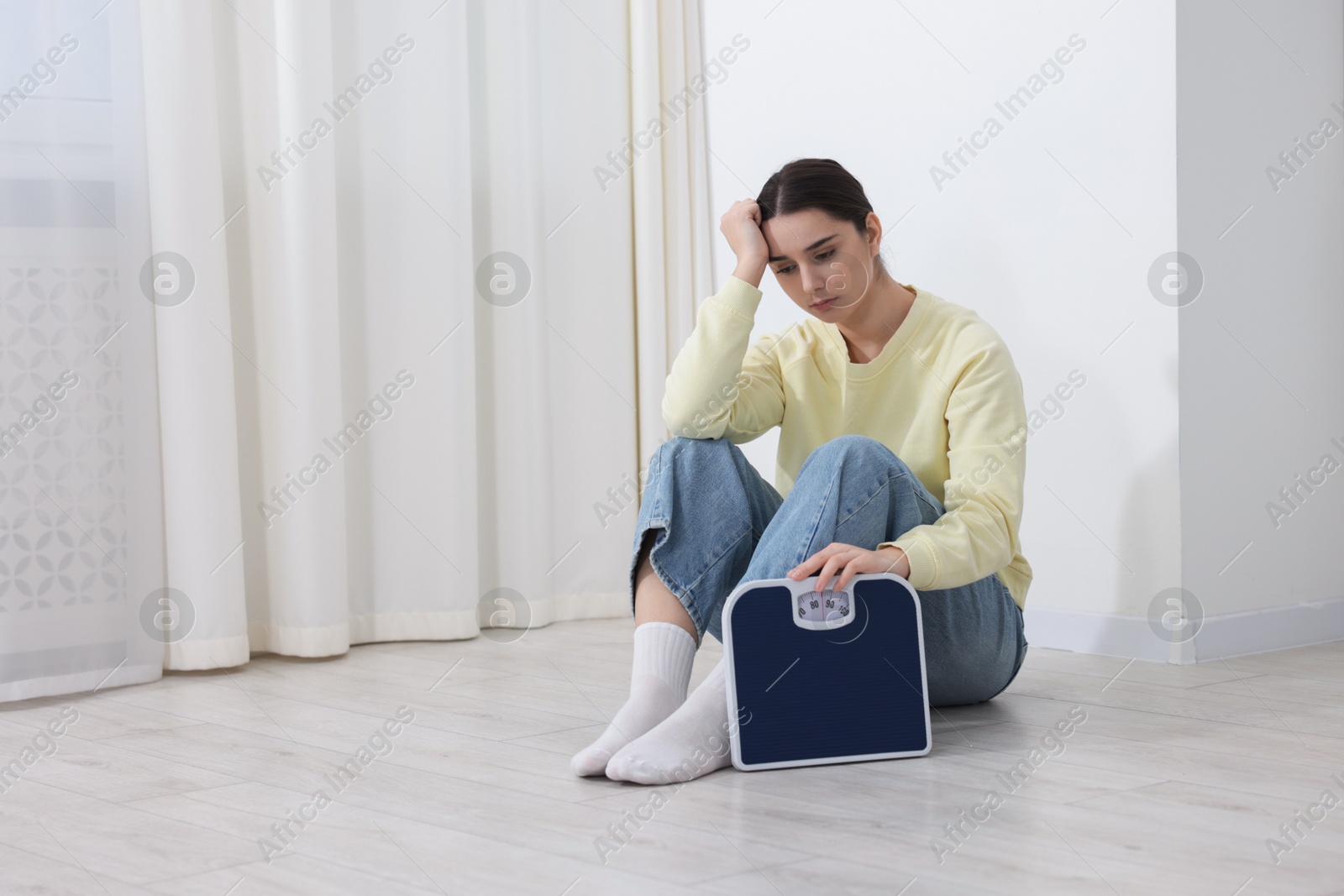 Photo of Depressed woman with scales on floor at home, space for text. Bulimia problem