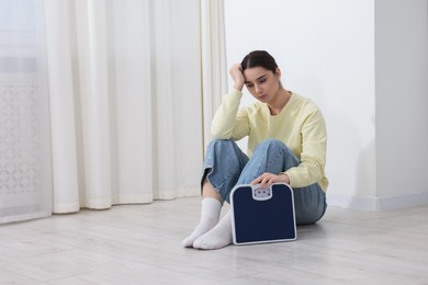 Photo of Depressed woman with scales on floor at home, space for text. Bulimia problem