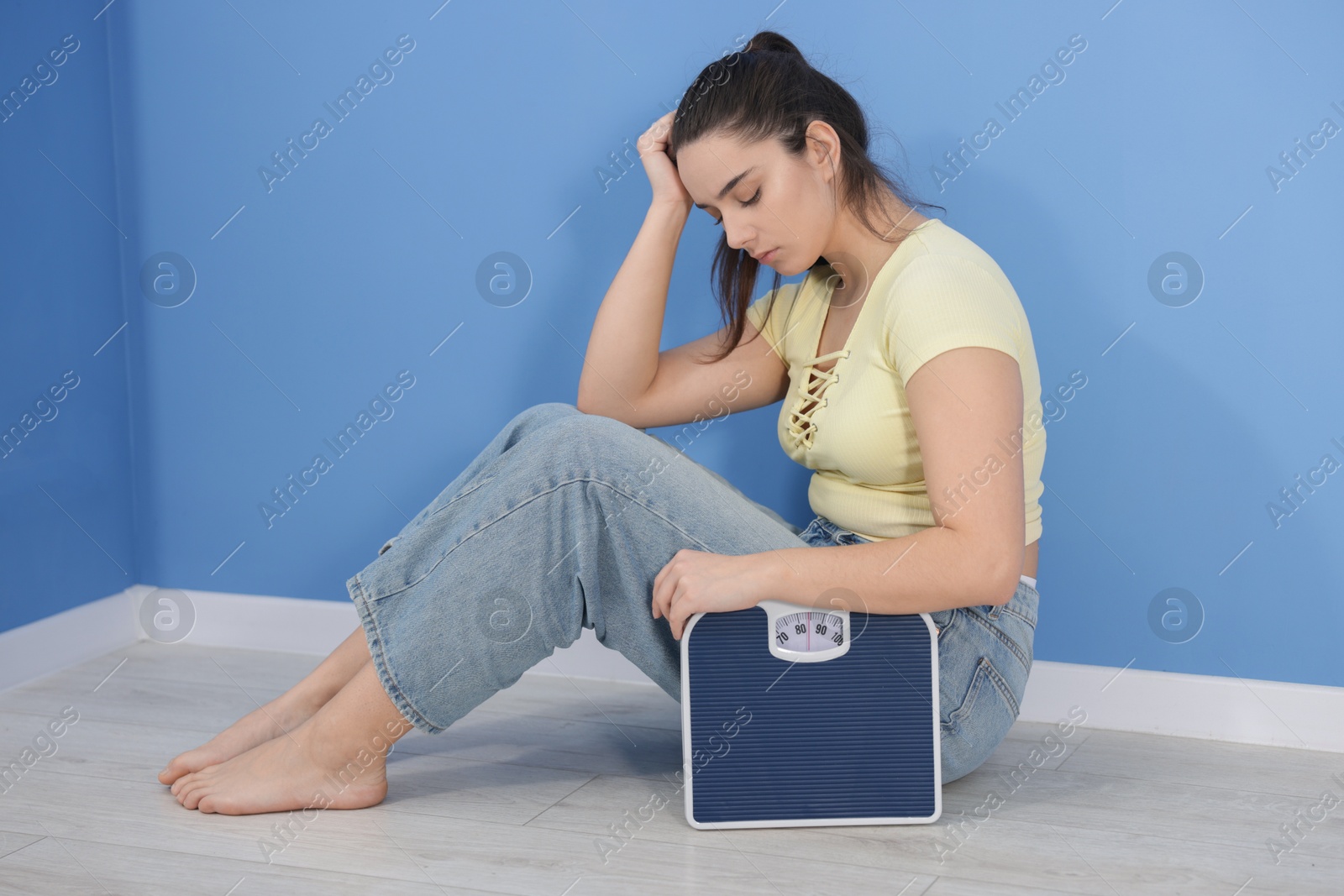 Photo of Depressed woman with scales on floor at home. Bulimia problem