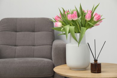 Photo of Bouquet of beautiful tulips in vase and reed diffuser on wooden table indoors, space for text