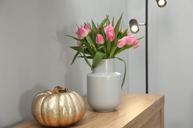 Photo of Bouquet of beautiful tulips in vase and decorative pumpkin on wooden cabinet near grey wall indoors